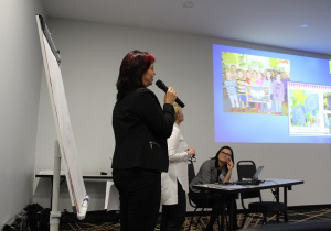 Zdjęcie przedstawia salę, nauczyciela, który opowiada podczas konferencji o projekcie.